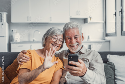 Happy retired family couple using mobile phone for video call together, talking to relations, getting good news, having fun, smiling and laughing. Carefree mature pensioners chatting online on cell.