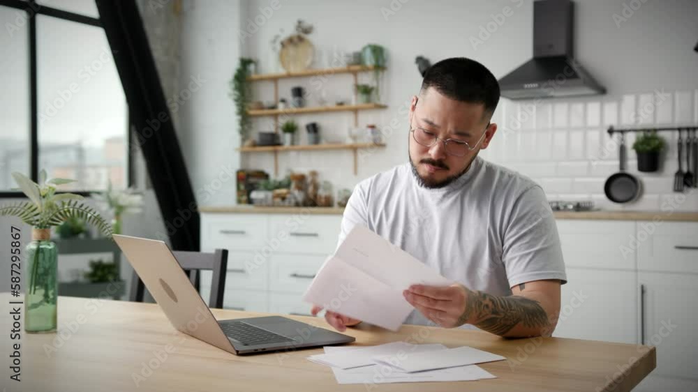 30s Man Checking Paperwork Using Laptop. Asian entrepreneur working with paper documents invoice at home office. 30s Man Checking Paperwork Using Laptop. Asian entrepreneur working with paper documents invoice at home office.