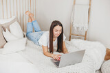 Girl advertising manager works at home with a laptop lying on a white bed