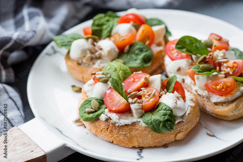 Bruschetta (sandwiches) with cherry tomatoes, mozzarella cheese and herbs on a stylish plate on a dark background. A traditional Italian snack. Bruschetta (sandwiches) with cherry tomatoes, mozzarella cheese and herbs on a stylish plate on a dark background. A traditional Italian snack.