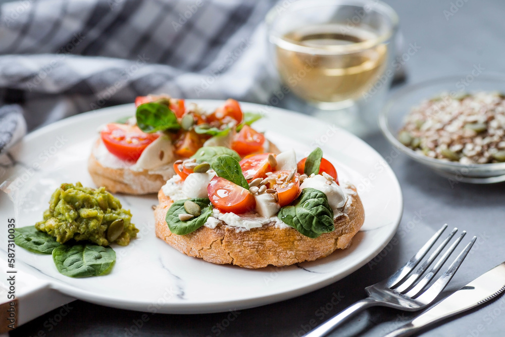 Bruschetta (sandwiches) with cherry tomatoes, mozzarella cheese and herbs on a stylish plate on a dark background. A traditional Italian snack. Bruschetta (sandwiches) with cherry tomatoes, mozzarella cheese and herbs on a stylish plate on a dark background. A traditional Italian snack.