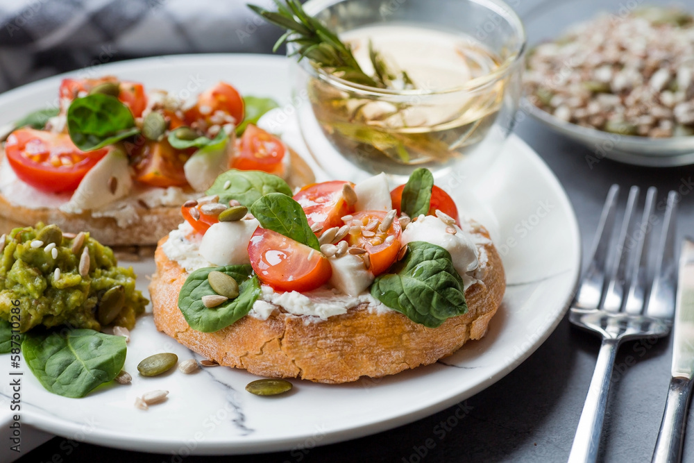 Bruschetta (sandwiches) with cherry tomatoes, mozzarella cheese and herbs on a stylish plate on a dark background. A traditional Italian snack.