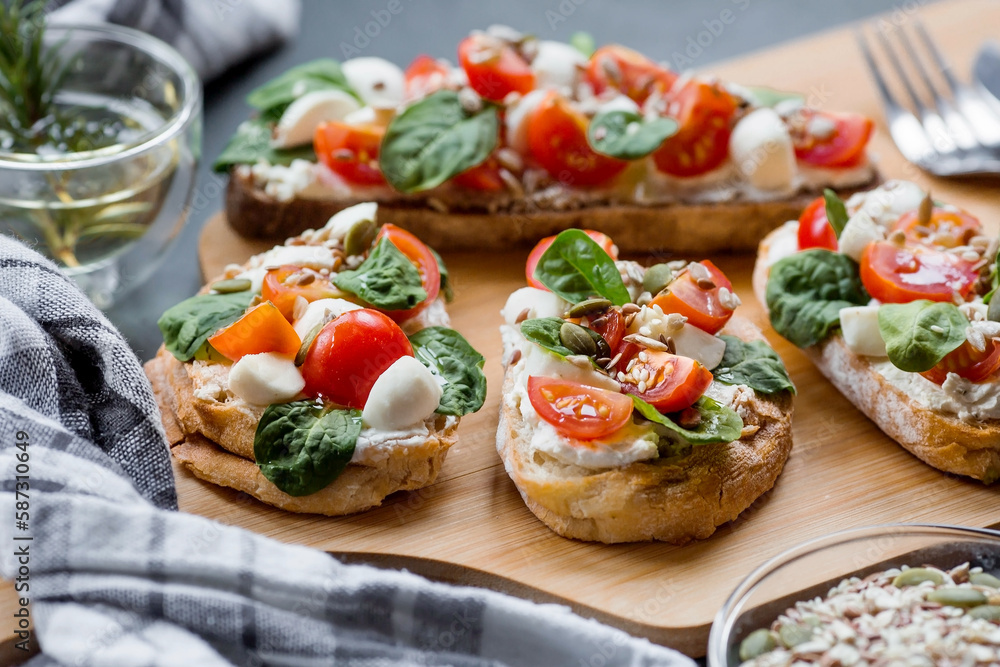 Bruschetta (sandwiches) with cherry tomatoes, mozzarella cheese and herbs on a cutting board on a dark background. Traditional Italian snack. Bruschetta (sandwiches) with cherry tomatoes, mozzarella cheese and herbs on a cutting board on a dark background. Traditional Italian snack.