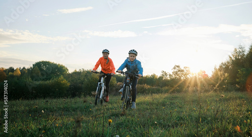 Mother and son ride a bike. Happy cute boy in helmet learn to riding a bike in park on green meadow in autumn day at sunset time. Family weekend. 