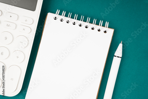 The Blank Spiral notebook and pen with calculator on green background, top view, flat lay.