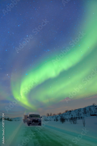 SUV rides on a winter forest road - A car in a snow-covered road among trees and snow hills - Northern lights or Aurora borealis in the sky over Tromso fjords - Tromso, Norway