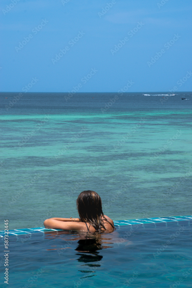 Woman in the infinity pool of a hotel while watching the sea