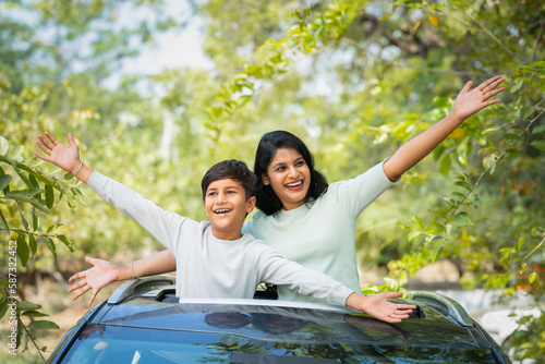 Happy smiling mother with kid feeling nature fresh air by shouting on car sunroof - concept of family bonding, leisure active and traveling. photo