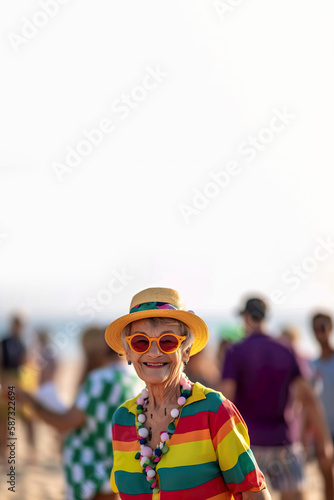 A happy elderly woman dressed in rainbow colors having fun at the beach party. Generative AI illustration. 