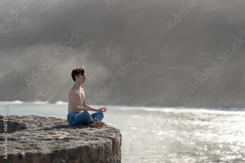 Shirtless teenager boy meditating in lotus pose