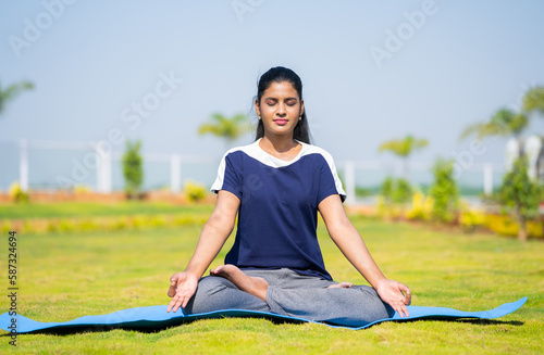 Young woman doing yoga or meditation with eyes closed at park - concept of relaxation, self care and healthy lifestyle