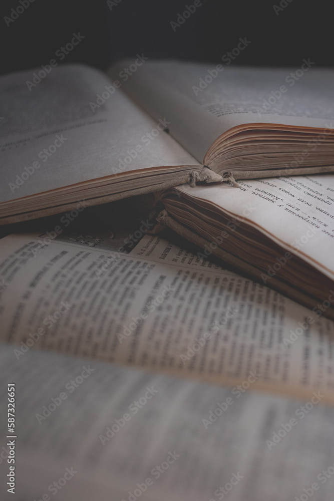 Obraz premium A stack of old books with frayed spines and yellowed pages. Book pages are yellow from old age. Many books. Source of knowledge. Old library. Vintage background. Yellow pages. An open book. 