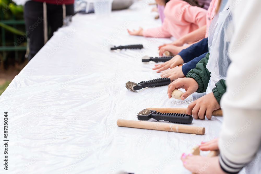 Fototapeta premium Kids cooking, roll out the dough and making matzah for Jewish holiday Passover Pesach at culinary master class for children outdoor in park. 