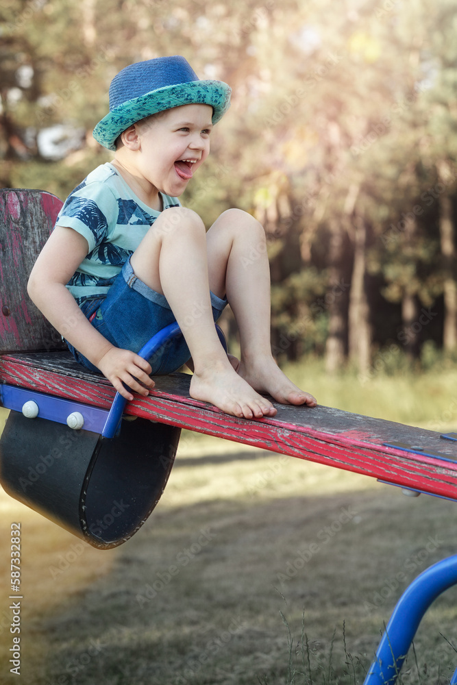 A little cheerful boy in blue clothes is sitting high on a balance swing and is very happy. A little cheerful boy in blue clothes is sitting high on a balance swing and is very happy.