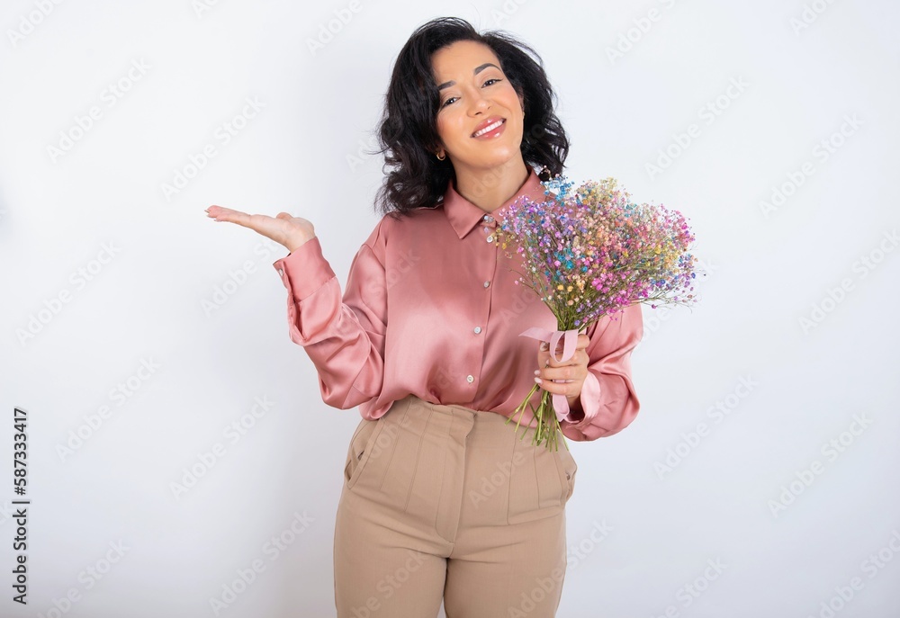 young woman holds big bouquet of nice flowers over white background smiling cheerful presenting and pointing with palm of hand looking at the camera. young woman holds big bouquet of nice flowers over white background smiling cheerful presenting and pointing with palm of hand looking at the camera.