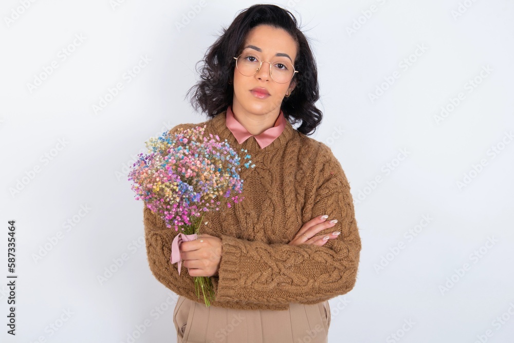 Confident young woman holds big bouquet of nice flowers over white background with arms crossed looking to the camera Confident young woman holds big bouquet of nice flowers over white background with arms crossed looking to the camera