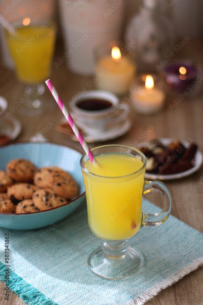 Plate of chocolate pralines, bowl of cookies, cups of tea, glasses of juice and lit candles on the table. Selective focus. Plate of chocolate pralines, bowl of cookies, cups of tea, glasses of juice and lit candles on the table. Selective focus.