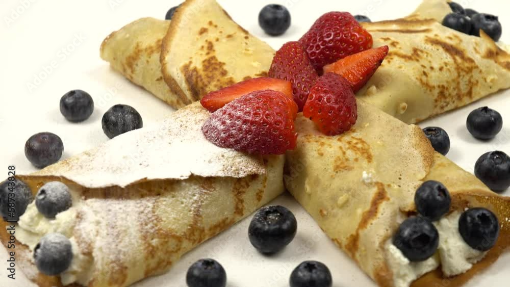 Sprinkling of powdered sugar on freshly baked pancakes crepes with cottage cheese filling, garnished with fresh strawberries and blueberries Sprinkling of powdered sugar on freshly baked pancakes crepes with cottage cheese filling, garnished with fresh strawberries and blueberries