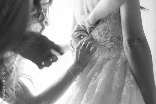 foto in bianco e nero del dettaglio di mani che si accingono a chiudere i bottoni di un abito appena indossato da una sposa  photo