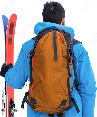 Rear view of skier with backpack holding skis
