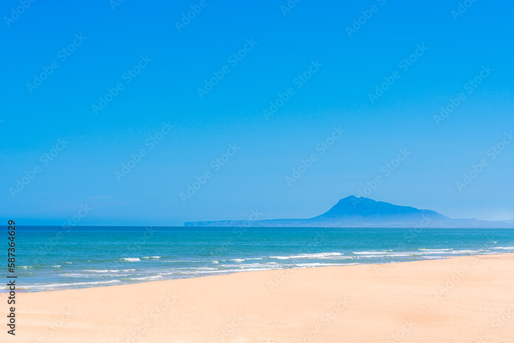A beach with a blue sky and a mountain in the background