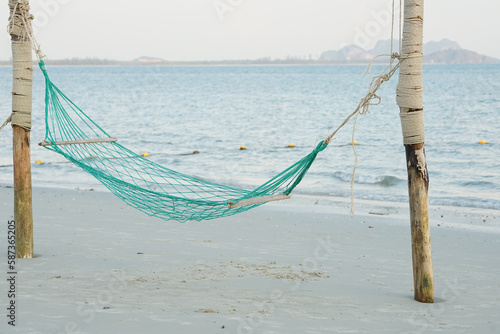 Empty swing weaved by rope hanging on the wooden poles on the beach with seascape background