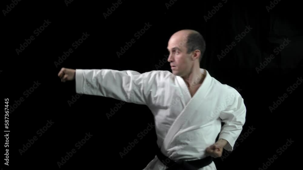 On a black background, an adult athlete performs formal karate exercises On a black background, an adult athlete performs formal karate exercises