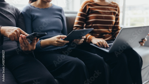 Closeup group of adults friends sitting on couch with hands modern smartphone tablet business startup friendship teamwork concept coworking people project coworking process studio.