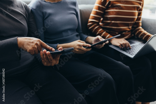 Closeup group of adults friends sitting on couch with hands modern smartphone tablet business startup friendship teamwork concept coworking people project coworking process studio.