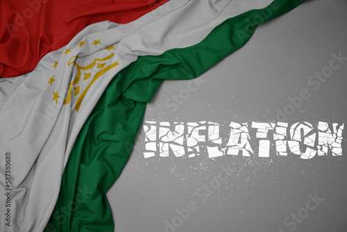 waving colorful national flag of tajikistan on a gray background with broken text inflation. 3d illustration