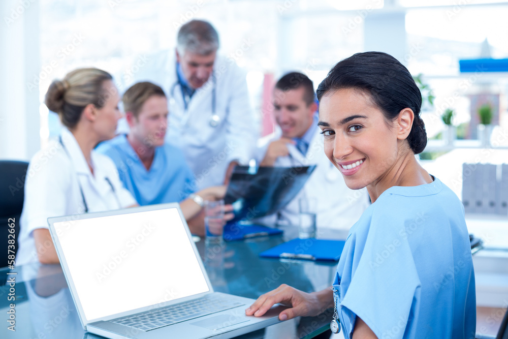 Beautiful smiling doctor typing on keyboard with her team behind