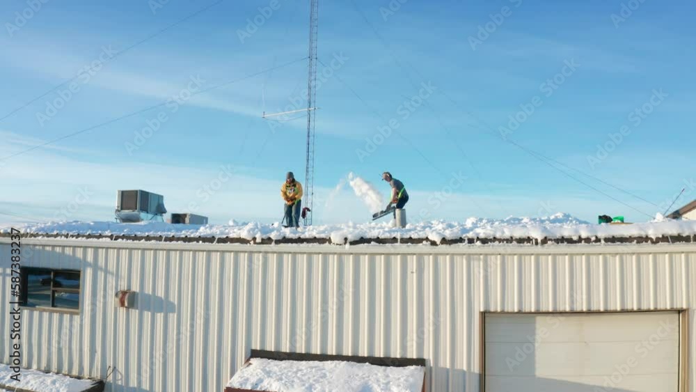 Two men shoveling the snow off the roof of a local business warehouse in Soldotna, Alaska Two men shoveling the snow off the roof of a local business warehouse in Soldotna, Alaska