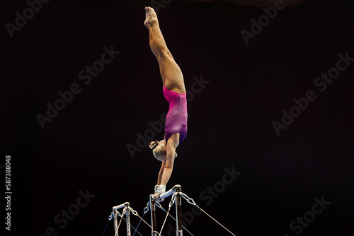 female gymnast performing exercise on uneven bars on black background, sports summer games photo