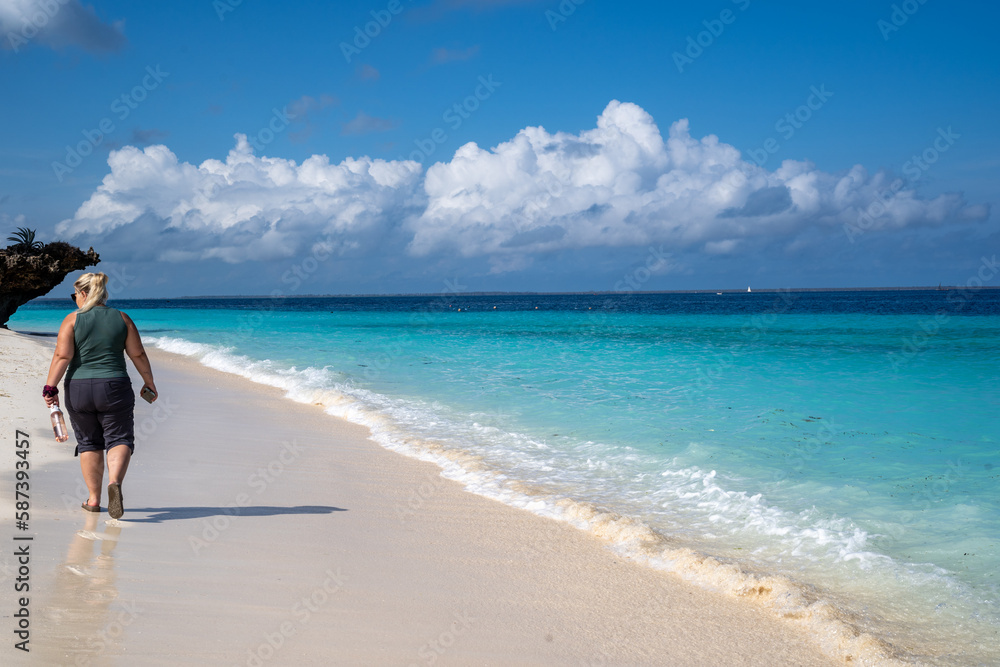 Blonde woman walks away from the camera while walking on a beach in Zanzibar, Tanzania Blonde woman walks away from the camera while walking on a beach in Zanzibar, Tanzania