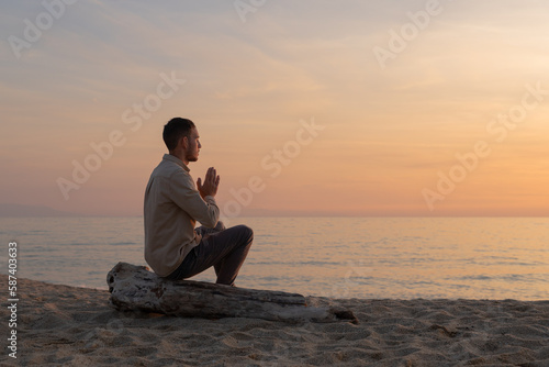 young man in a shirt, making a prayer in a sunset on the beach photo