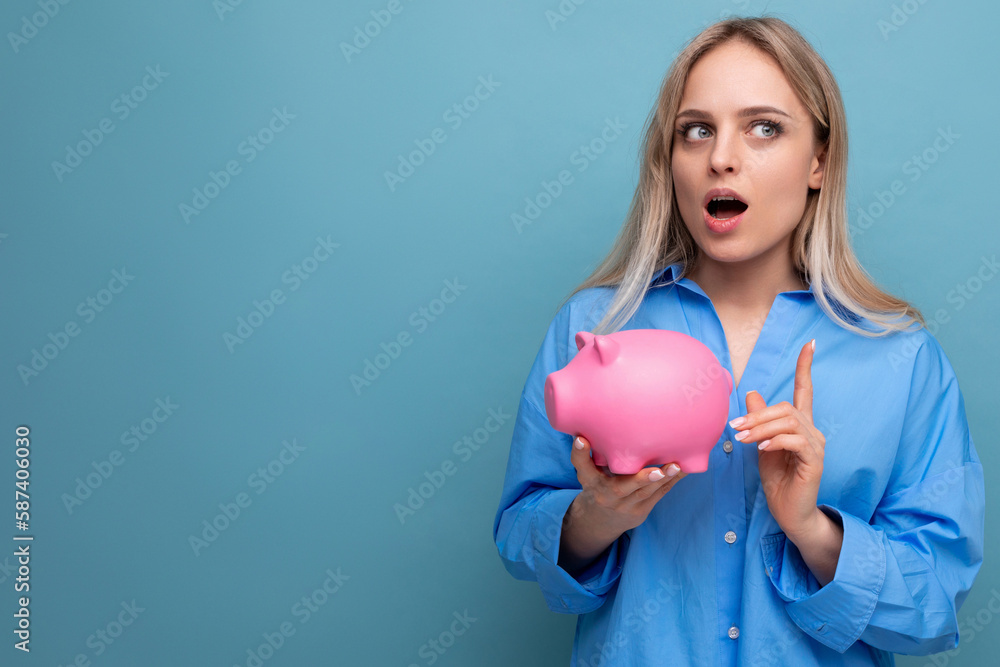 pensive blond girl holding a piggy bank with a stock thinks where to spend money on a blue isolated background pensive blond girl holding a piggy bank with a stock thinks where to spend money on a blue isolated background
