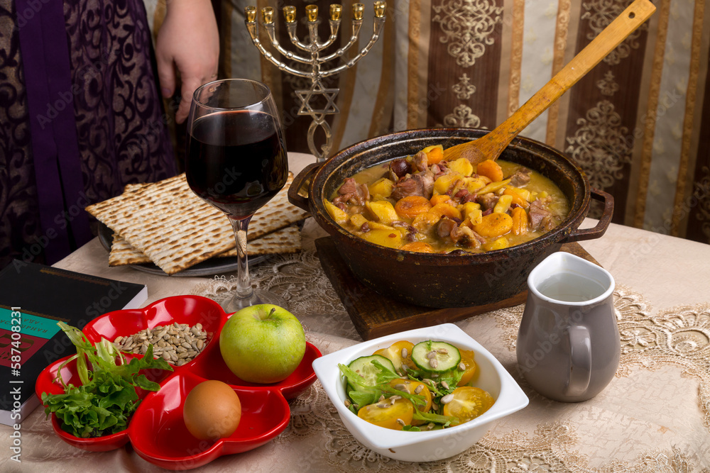 A set table for the Passover Seder with matzah, wine, maror and a hot cholent for the meal and menorah.