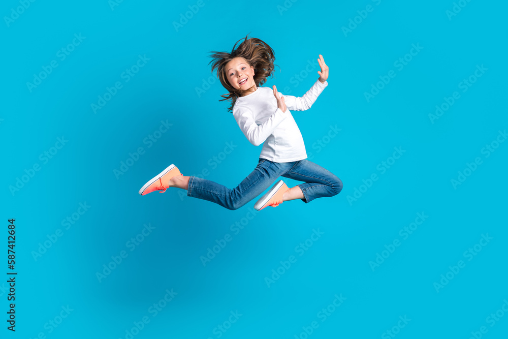Full length photo of good mood positive schoolgirl dressed white shirt jeans sneakers flying having fun isolated on blue color background