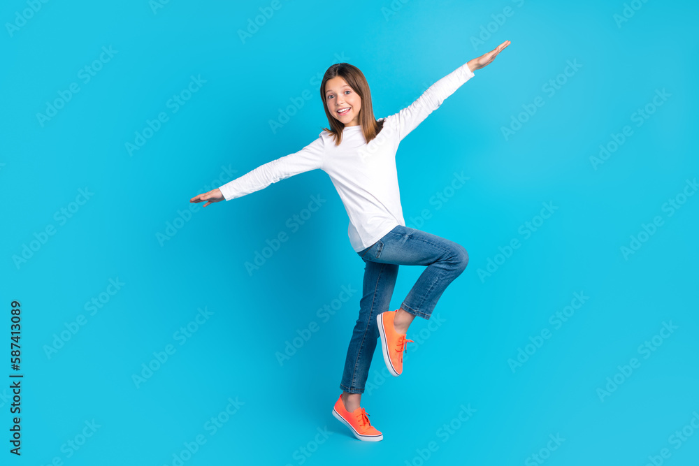 Full length photo of good mood schoolgirl dressed white shirt jeans sneakers hold arms like wings isolated on blue color background