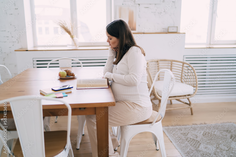 Chile bearing woman sitting at table and reading book in kitchen Chile bearing woman sitting at table and reading book in kitchen