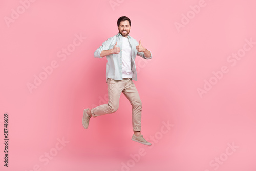 Full length photo of cool confident guy dressed teal shirt jumping high thumbs up isolated pink color background