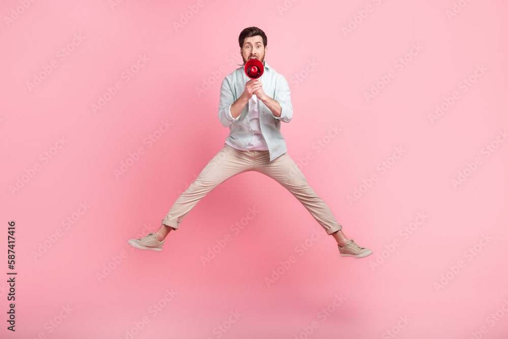 Full length photo of cheerful funky guy dressed teal shirt jumping high screaming loudspeaker isolated pink color background Full length photo of cheerful funky guy dressed teal shirt jumping high screaming loudspeaker isolated pink color background