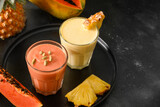 Fruits Pineapple and Papaya lassie or smoothie on black background. Traditional healthy vegan Asian beverage. Copy space.