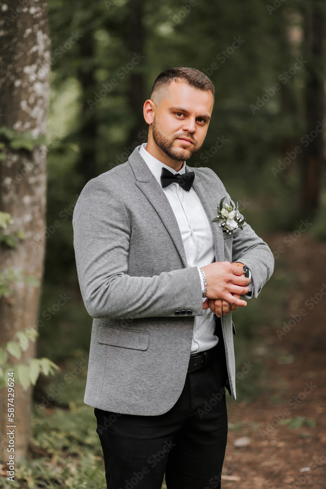 stylish groom adjusted his watch looking into camera lens. Luxury expensive watch on hand. Gray jacket, white shirt, ankle boots made of fresh flowers. Photo details stylish groom adjusted his watch looking into camera lens. Luxury expensive watch on hand. Gray jacket, white shirt, ankle boots made of fresh flowers. Photo details
