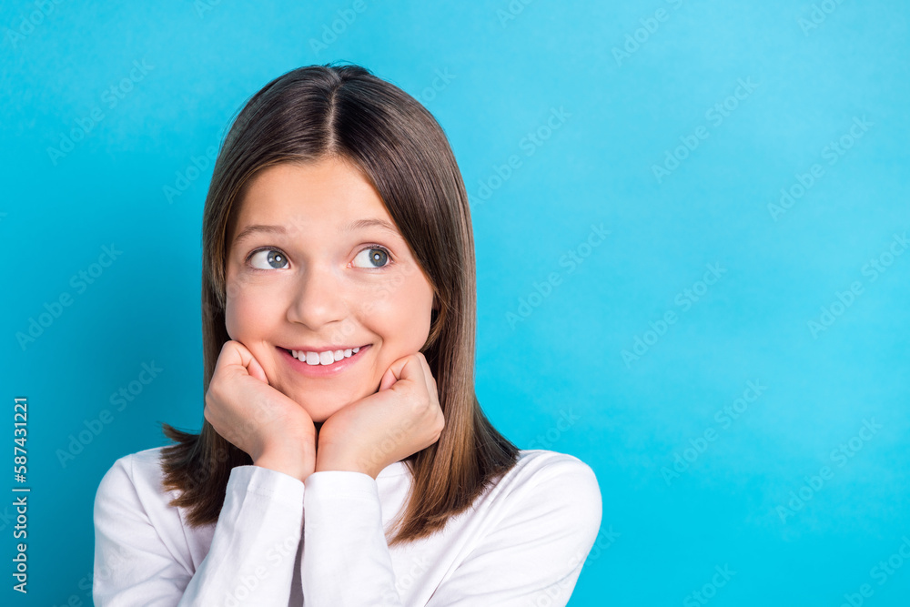 Photo portrait of small schoolkid girl fists touch cheeks look empty space dressed stylish white garment isolated on blue color background Photo portrait of small schoolkid girl fists touch cheeks look empty space dressed stylish white garment isolated on blue color background