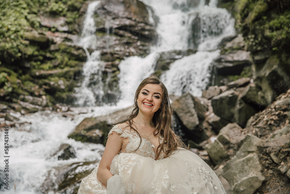Portrait of a happy bride with curly hair near a waterfall. Bride and groom. Wedding photo session in nature. Photo session in the forest of the bride and groom.