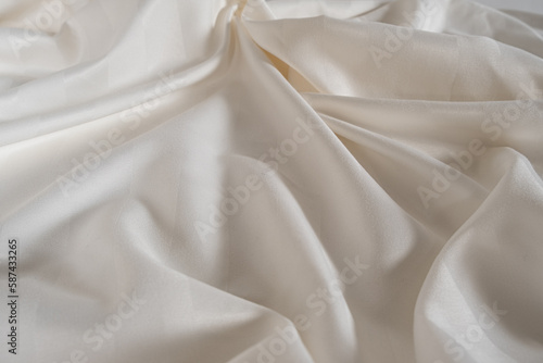 Satin crumpled fabric of light milky color, top view. Natural bed linen, sheets, abstract background of luxury fabric, wavy folds