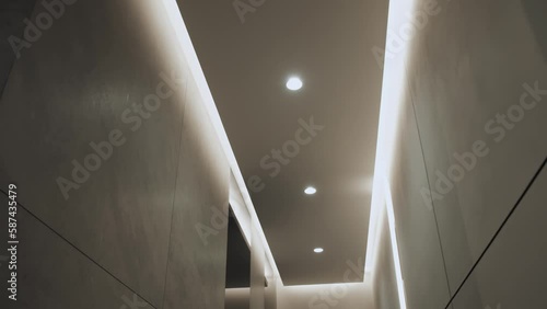 Dolly shot of round modern ceiling lamp in minimalist interior with hidden LED backlight. Minimalist Interior with lighting equipment. Contemporary modern lamp. Luxury Chandelier, slow motion.