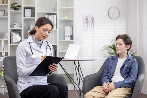 A schoolboy boy at a doctor's appointment, a female doctor writes down the anamnesis of a patient, a teenager at a female pediatrician's appointment.