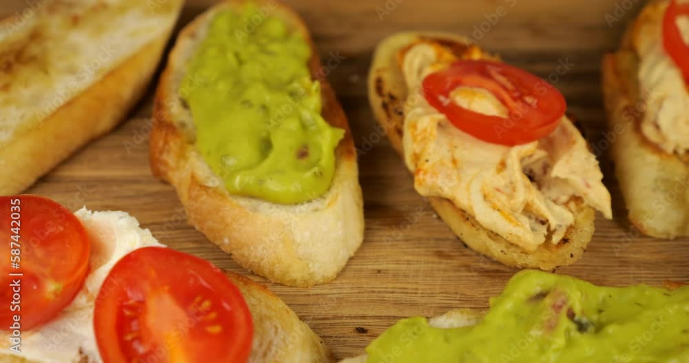 Hummus, guacamole and cream cheese spread with fresh tomatoes on toasted bread. Assorted snacks on a wooden cutting board. Food for vegans. Hummus, guacamole and cream cheese spread with fresh tomatoes on toasted bread. Assorted snacks on a wooden cutting board. Food for vegans.